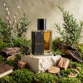 Perfume bottle labeled 'Wildwoods' surrounded by natural elements like plants and stones.