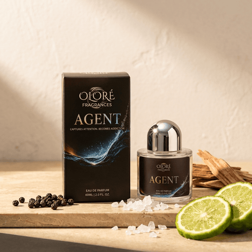Oloré Fragrances Agent Eau de Parfum bottle and its retail box, styled on a wooden board with salt, peppercorns, and lime slices against a textured beige wall.