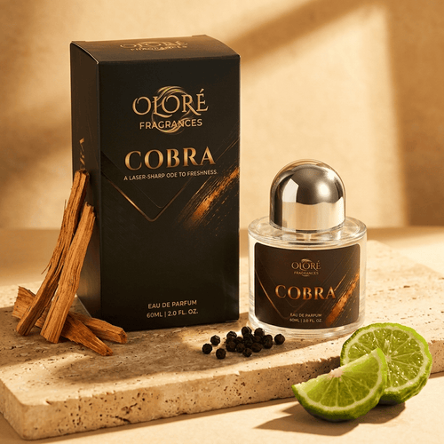 Oloré Fragrances Cobra Eau de Parfum bottle and its black packaging box, styled on a stone slab with cinnamon sticks, peppercorns, and lime slices against a warm beige background.